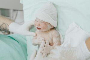 A newborn baby just delivered, attended by medical staff wearing gloves in a hospital setting.